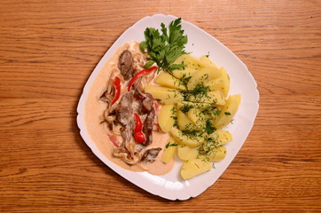 Beef meat stewed with potatoes, carrots and spices in ceramic pot on wooden background