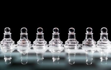 Glass pawn chess pieces or figures arranged in a row reflecting in glass chessboard. Isolated on black background with copyspace. Concept of order.