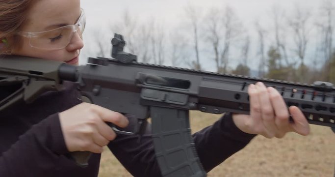 Female in safety glasses shoots an automatic rifle