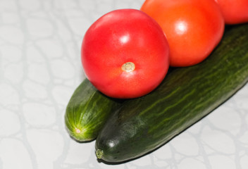 Fresh cucumbers and tomatoes as a whole on a light background.