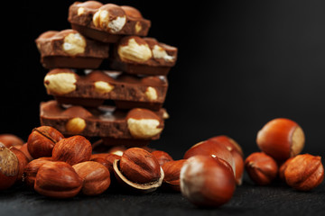 Chocolate with hazelnuts in the form of a tower on a dark background, surrounded by nuts in the shell and peeled.