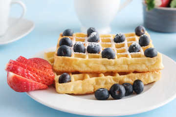 Freshly sung homemade Viennese or Belgian waffles with fresh strawberries and blueberries on a blue...