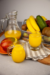 Fresh mango juice. Fruit basket on the table. Refreshing summer drink, orange juice. A glass on the table. Fruits are banana, kiwi, avocado and others. Vitamin nutrition. Vegan Food. 