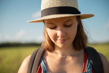 Young woman in straw hat standing in grass field looking down in sunlight