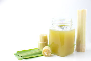 Fresh squeezed sugar cane juice in clear glass with cut pieces cane on white background.
