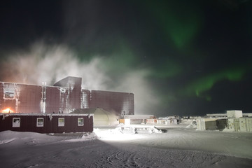 Blizzard snow storm and Northern Lights dancing over an ore processing plant in arctic region...