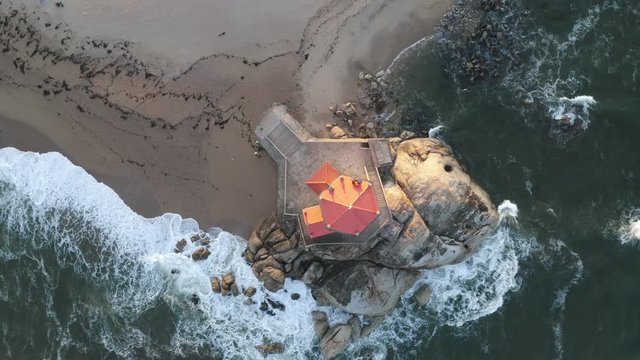 Capela Senhor da Pedra most beautiful chapel drone aerial top view from above on a beach near the ocean with waves, in Portugal