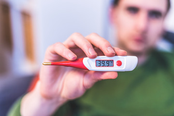 Flu and corona concept: Man is holding a fever thermometer in his hand, close up - obrazy, fototapety, plakaty