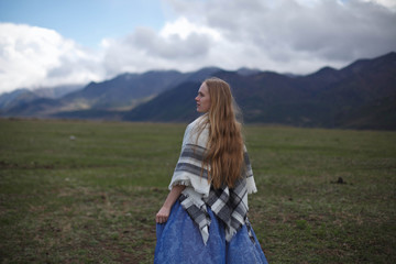 a girl walks in a field on a background of snow-capped mountains than the Chemal district