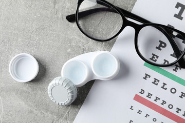 Glasses, case for contact lenses and eye test chart on grey background, top view
