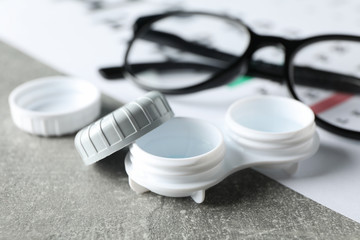 Glasses, case for contact lenses and eye test chart on grey background, close up