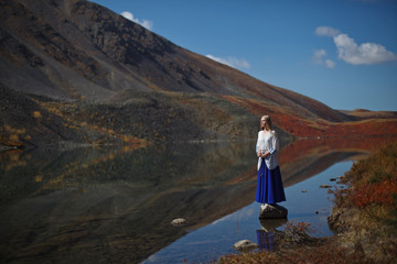 beautiful girl in a blue skirt stands on a bridge by the lake