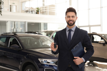 Salesman with key and clipboard in car salon