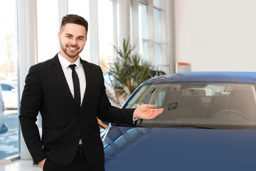 Young salesman near new car in dealership