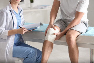 Female orthopedist examining patient with injured knee in clinic, closeup