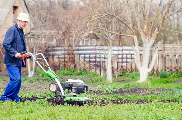 A man plows the land with a cultivator in a spring garden