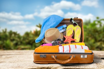 Retro suitcase with travel objects on wooden desk in beach background