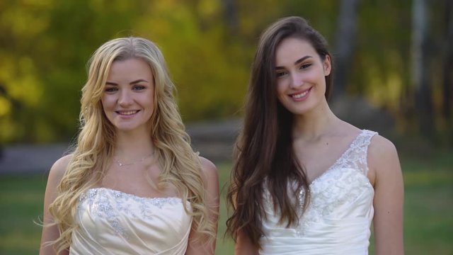 Two brides is having fun and laughing in the sunshine against landscape of autumn nature. Brunette and blonde women