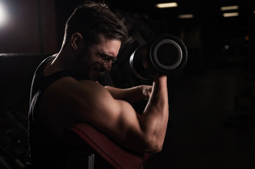 Fototapeta na wymiar A handsome man with glasses doing an exercise for biceps with a barbell. The guy is engaged in bodybuilding. Trainer in the gym with muscular arms.