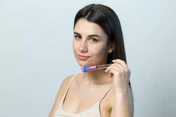 Close-up of a young girl in a light top on a white background making a facial make-up. A pretty woman holds a cosmetic brush near her face and smiles.