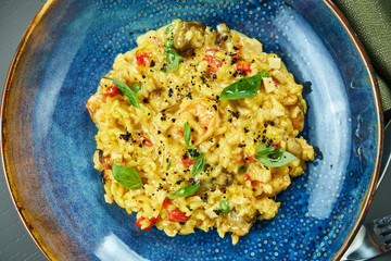 The classic dish of Italian cuisine - risotto with seafood, vegetables and spices in a blue bowl on a wooden background. Top view. Close up