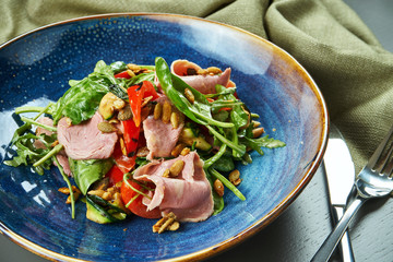 Appetizing warm salad with veal grill and vegetables, spinach and pine nuts in a blue bowl on wooden background. Healthy eating. Close up, copy space, selective focus