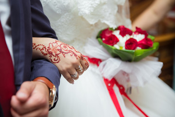 Let's get into the groom's arms. The bride holds a red bouquet in her hand. Hands and fingers are...