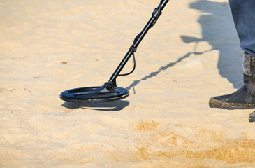 Close up of a man with a metal detector on the shore of a sandy beach. - 328125806