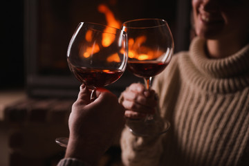 Couple with glasses of red wine near fireplace, closeup