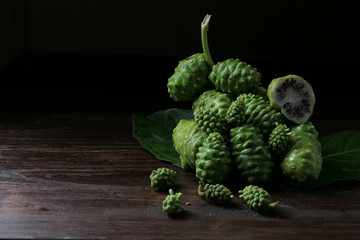 Noni fruit, herbs and sliced on wood, on a black background. Dark tones, rich in nutrients. Antioxidants.