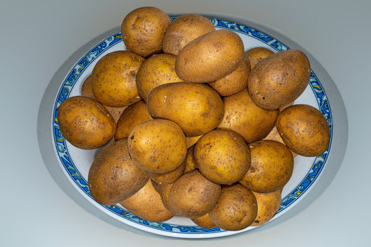 Diverse ungesch&auml;lte Kartoffeln auf einem Teller vor grauem Hintergrund