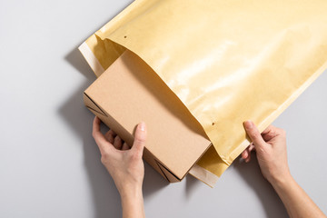 Woman hands puting  cardboard box inside of large postal envelope