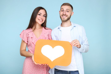 Happy young couple with paper heart on blue background