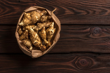 Several Jerusalem artichoke tubers in a paper bag on a wooden table with copy space. Helianthus tuberosus. Top view