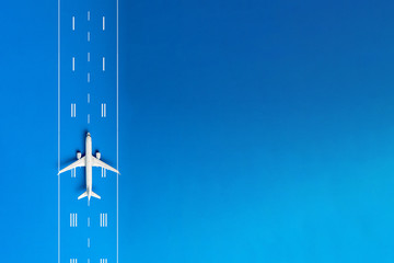 The passenger plane on airport runway and blue background with empty space for text. Top view, copy space - obrazy, fototapety, plakaty