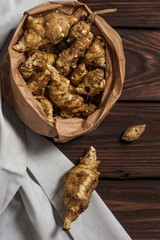Several Jerusalem artichoke tubers in a paper bag on a wooden table with copy space. Helianthus tuberosus. Top view. Vertical orientation