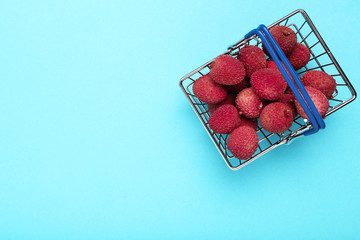 Tasty lychee in shopping basket on blue background