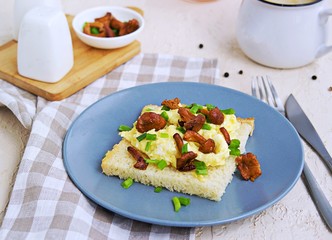 Tender scramble omelet on crispy white bread toast with fried chanterelles on a gray plate on a light concrete background.