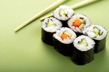Vegetarian sushi roll set with vegetable filling and chopsticks on a green background