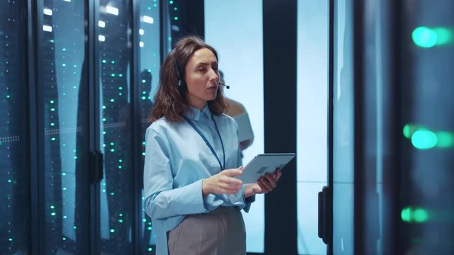 Beautiful IT server admin woman inspecting high secure racks of server cabinet using digital tablet. Man behind her getting ready to make surprise. Valentine's Day.