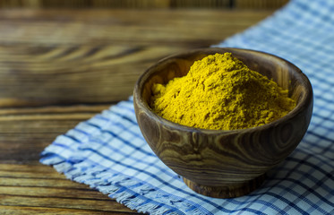 Turmeric powder in a wooden bowl on a blue napkin and a wooden background. Turmeric close -up. Banner with a copy of the space.