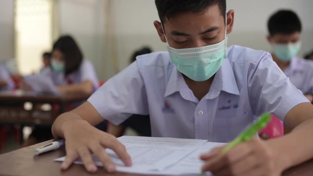 Asian high school students in a white school uniform wearing the masks to do final exams in the midst of Coronavirus disease 2019 (COVID-19) epidemic.