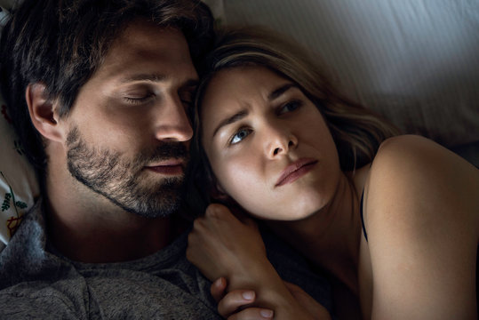 Close-up Of Scared Woman Sleeping With Her Husband On Bed