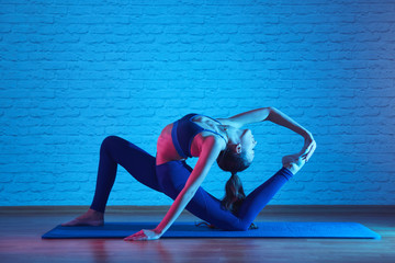 Flexible plastic girl doing pilates exercises on mat in yoga studio, body stretching pose