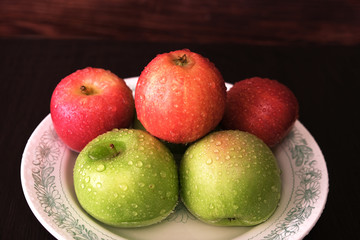 red and green apples in drops of water on a plate