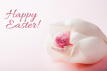 Pink colored egg in orchid flower on white background with sign Happy Easter. Easter spring concept, card.