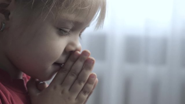 little daughter girl makes a wish prayers bedtime religion concept . prayer child indoors lifestyle praying by bed front of window