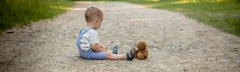 Little boy playing with teddy bear on the footpath
