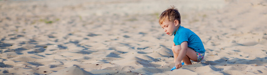 Boy playing on beach. Child play at sea on summer family vacation. Sand and water toys, sun protection for young child. Little boy digging sand, building castle at ocean shore. © volody10