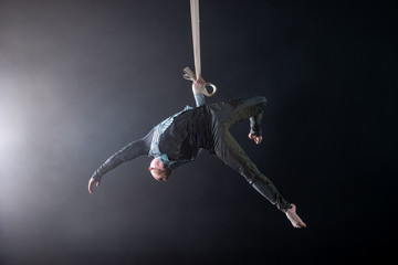 Circus artist on the aerial straps with costume on the black and smoked background.